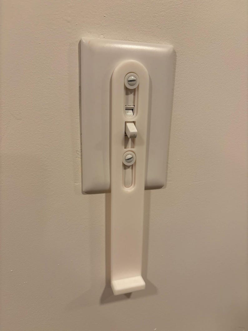 Puede incluir: Una placa de cubierta para interruptor de luz de pl&aacute;stico blanco con un brazo de extensi&oacute;n vertical integrado y un peque&ntilde;o estante en la parte inferior. El dispositivo se monta sobre un interruptor de palanca est&aacute;ndar para accionarlo.