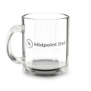 Puede incluir: Una taza de vidrio transparente con asa. La taza tiene las palabras "Midpoint Dad" impresas en gris en el lateral. La taza está vacía y se encuentra sobre una superficie blanca.