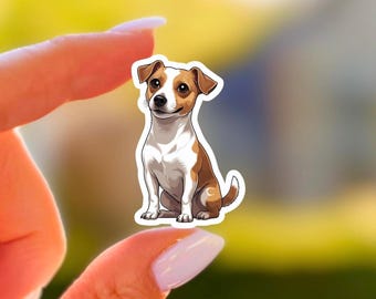 May include: A sticker featuring a cartoon Jack Russell Terrier dog. The dog is depicted in a sitting position with brown and white markings, a smiling expression, and a white outline. The sticker is held between two fingers against a blurred background.