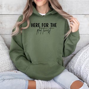 May include: A green hooded sweatshirt with the text "HERE FOR THE PLOT TWIST" printed in black.
