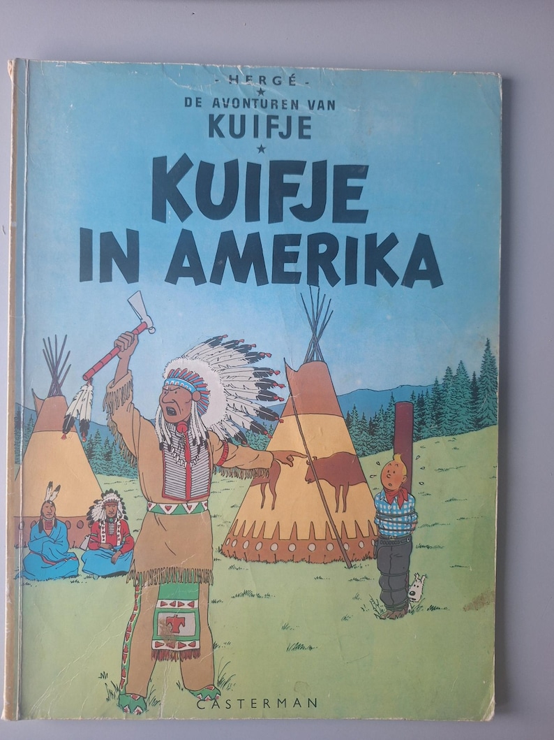 Puede incluir: Una portada de c&oacute;mic vintage titulada "KUIFJE IN AMERICA" con una figura nativa americana sosteniendo un tomahawk. La portada tiene ilustraciones de tipis, un personaje atado y un fondo de bosque. El libro es de Herg&eacute;.