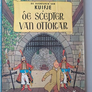 May include: A vintage comic book cover featuring a cartoon illustration. The title "De Scepter Van Ottokar" is displayed on a yellow scroll. The cover depicts a man in a tan coat running, with two guards and a dog.