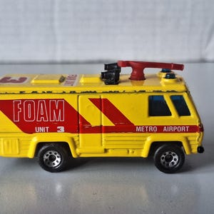 May include: A yellow toy fire truck with red accents, labeled "FOAM UNIT 3" and "METRO AIRPORT." The toy has black wheels and a red nozzle on top. A classic collectible toy.