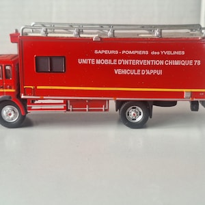 May include: Red fire truck toy model with a white ladder on top and the text "SAPEURS-POMPIERS des YVELINES UNITE MOBILE D'INTERVENTION CHIMIQUE 78 VEHICULE D'APPUI" on the side.