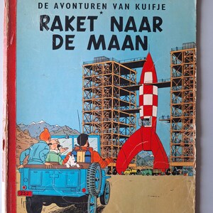 May include: Vintage comic book cover featuring a red and white rocket, blue jeep, and the text "RAKET NAAR DE MAAN." The cover has a blue sky background and illustrations of a rocket launch site.