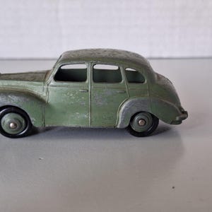 Può includere: Un'auto giocattolo vintage verde sbiadito. Il modello pressofuso presenta quattro porte, ruote nere e dettagli argentati. L'auto in miniatura è una replica di una classica berlina.