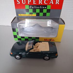 Può includere: Un'auto giocattolo decappottabile Mercedes 500 SL verde scuro con interni beige, presentata davanti alla sua scatola Supercar Collection. La scatola è rossa, nera e gialla con la scritta "SUPERCAR Collection".