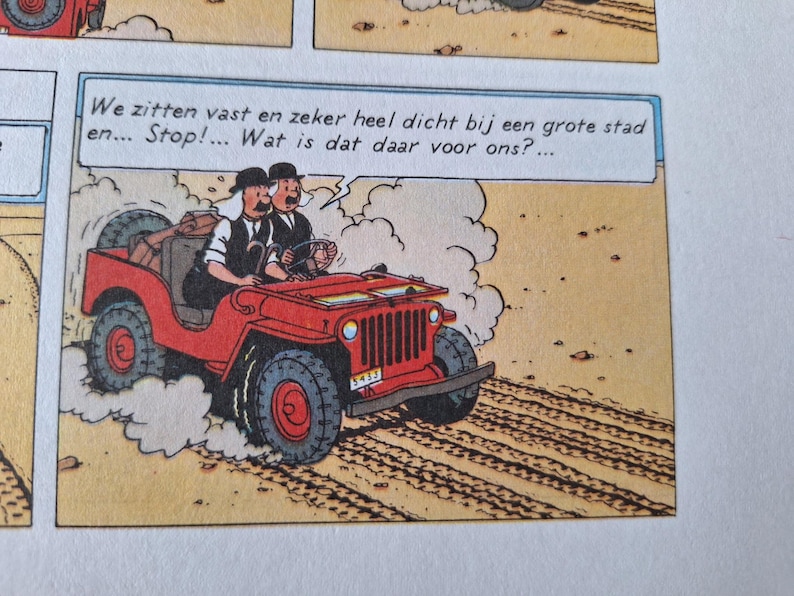 May include: Comic strip panel featuring two men in a red jeep driving on a dirt road. The jeep has large tires and a spare tire on the back. Text in a speech bubble reads, "We are stuck and very close to a big city... Stop!... What is that there for us?"