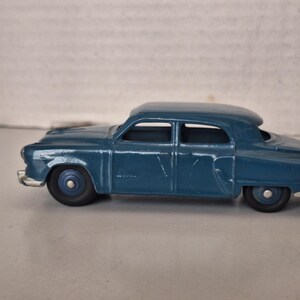 May include: A vintage-style blue die-cast toy car featuring a saloon body shape, four doors, and silver-coloured bumpers. The model has dark blue wheels with silver centres and a smooth, painted finish on the exterior metal body.