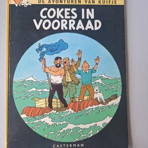 May include: A vintage comic book cover with a nautical theme. The cover shows three men and a dog on a raft at sea. The title "COKES IN VOORRAAD" is displayed, with the author's name "HERG&Eacute;" at the top. The background is dark blue.