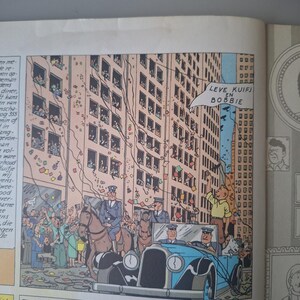 Puede incluir: Ilustraci&oacute;n de c&oacute;mic de una escena urbana con un coche azul vintage, personas y edificios. Confeti cae de las ventanas de un edificio alto. El texto en un bocadillo dice "LEVE KUIFJ EN BOBBIE".
