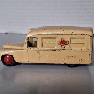 Può includere: Un'ambulanza giocattolo vintage color crema con un'emblema a croce rossa. I pneumatici neri hanno i mozzi rossi. Il design classico suggerisce un'epoca passata. Il giocattolo è in metallo.
