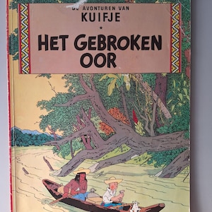 May include: A vintage comic book cover with the title "Het Gebroken Oor". The illustration shows a river scene with two people in a boat, and a dog. The book is by Herg&eacute;. The cover has a beige and brown color scheme.