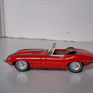 Op de afbeelding: Een rood model van een vintage cabriolet sportwagen met een lange motorkap, een beige interieur, een lage voorruit en zilveren spaakwielen met whitewall-banden. Het voertuig is voorzien van chromen bumpers en sierstrips aan de zijkant.