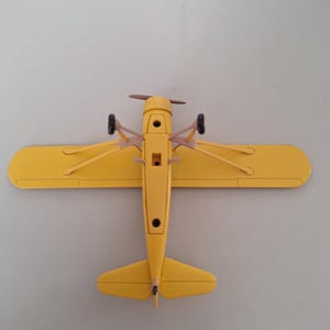 May include: A bright yellow toy aeroplane with a propeller and small wheels. The wings are extended, and the plane is viewed from above. The model aeroplane is a classic design, likely a vintage or retro style.