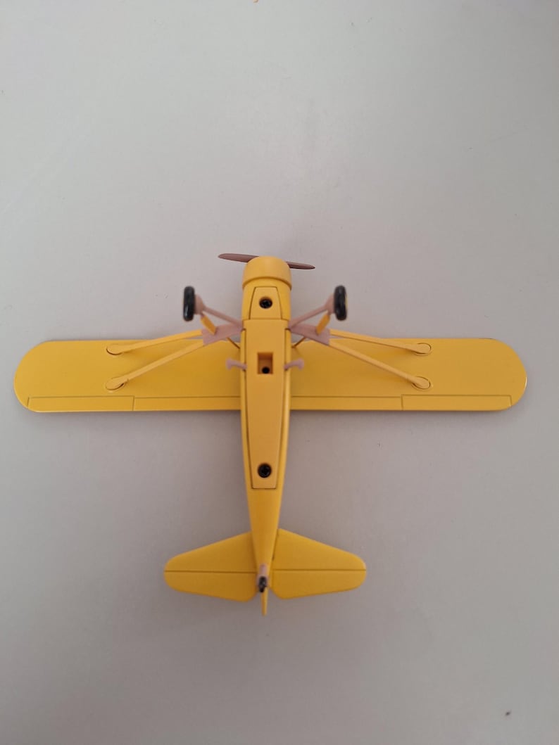 May include: A bright yellow toy aeroplane with a propeller and small wheels. The wings are extended, and the plane is viewed from above. The model aeroplane is a classic design, likely a vintage or retro style.