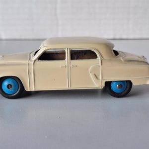 Könnte beinhalten: Ein Vintage-Spielzeugauto, eine cremefarbene Limousine mit blauen Rädern. Das Auto hat eine detaillierte Karosserie und ein klassisches Design.