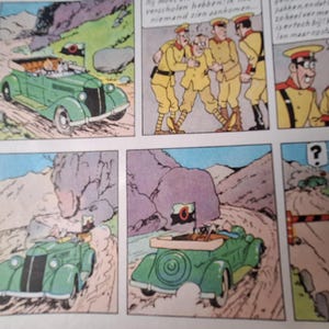 May include: Comic strip panels showing a green vintage convertible car on a winding road. The car has a flag with a black and white emblem. Other panels show characters in yellow uniforms and a mountain landscape.