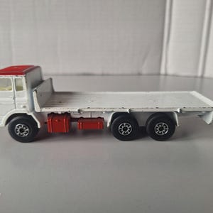 May include: White toy truck with a red cab and a flatbed. The truck has four black wheels and two red boxes on the flatbed.