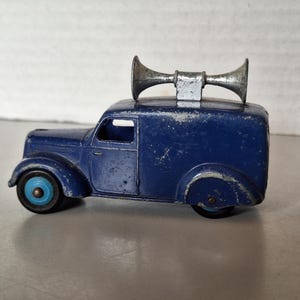 Può includere: Un furgoncino giocattolo blu in metallo pressofuso con un clacson doppio color argento montato sul tetto. Il veicolo presenta una carrozzeria blu scuro con segni di usura, un coprimozzo blu brillante e uno pneumatico nero. Design con cofano.