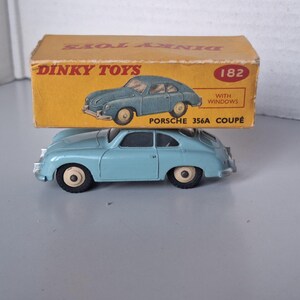 Pode incluir: Um carro de brinquedo em miniatura Dinky Toys Porsche 356A Coupé azul-claro com rodas cor de creme. O carro está posicionado abaixo da sua caixa de cartão amarela original, com o texto Dinky Toys, 182, With Windows e Porsche 356A Coupé.