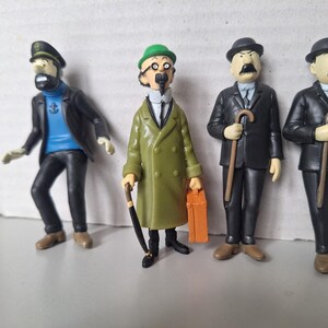 May include: Four figurines of characters from a comic book series. The figures include a captain in a black jacket and hat, a man in a green coat, and two men in black suits, all with distinctive features and accessories.
