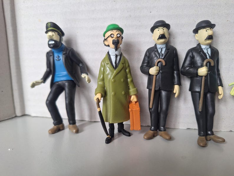 May include: Four figurines of characters from a comic book series. The figures include a captain in a black jacket and hat, a man in a green coat, and two men in black suits, all with distinctive features and accessories.