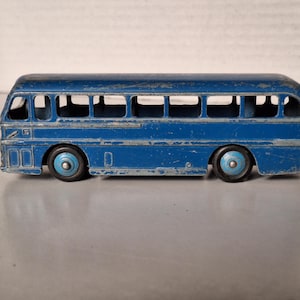 Könnte beinhalten: Ein alter blauer Spielzeugbus mit Gebrauchsspuren. Der Bus hat offene Fenster, zwei Achsen mit blau-schwarzen Rädern und ein abgerundetes Dach. Die Farbe weist Abnutzungserscheinungen auf, was ihm einen antiken Charme verleiht.