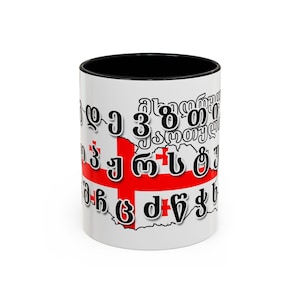 May include: White ceramic mug with a black rim. The mug features a black outline of the country of Georgia with the Georgian flag inside. The outline is filled with the Georgian alphabet in black.