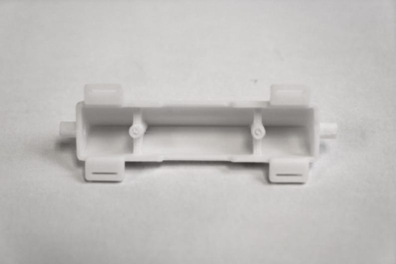 May include: White plastic battery holder with two compartments and tabs on either side.