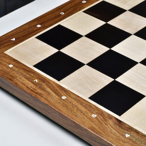May include: A close-up of a wooden chess board with a dark brown frame and a checkerboard pattern of black and light wood squares. The board's edge has white letter and number markings.