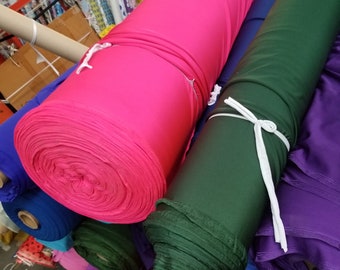 Puede incluir: Primer plano de rollos de tela en varios colores, incluyendo rosa, verde, azul y morado. Los rollos están apilados uno encima del otro y están listos para ser utilizados para proyectos de costura o manualidades.