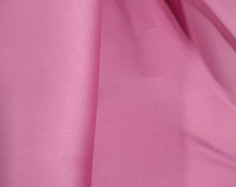 May include: A close-up of a smooth, pink fabric. The fabric is folded in half, with the fold line visible in the center of the image.