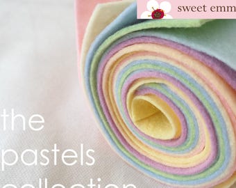 May include: A roll of pastel felt fabric in shades of pink, yellow, green, and blue. The felt is rolled up tightly and the ends are visible. The text "sweet emma jean" is printed on a white label attached to the roll.