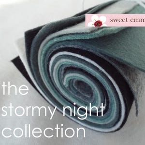 May include: A roll of felt fabric in shades of green, grey, and white. The fabric is rolled up tightly and the ends are visible. The text "the stormy night collection" is printed below the roll of fabric. The text "sweet emma jean" is printed in a pink banner above the roll of fabric.