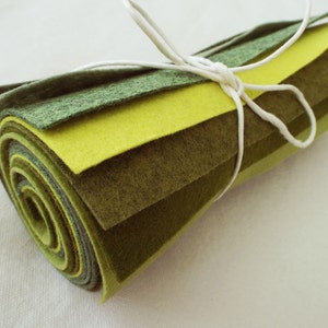 Puede incluir: Un rollo de tela de fieltro en tonos verdes y amarillos, atado con una cuerda blanca. El fieltro est&aacute; en capas en diferentes tonos de verde y amarillo, creando un efecto degradado.