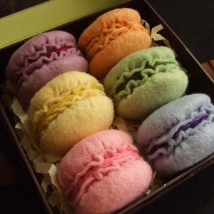 May include: Six felt macarons in a box. The macarons are in a rainbow of colors: purple, yellow, green, blue, pink, and orange.
