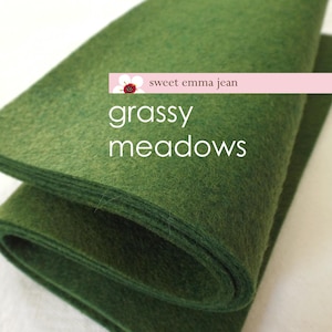 Può includere: Un rotolo di tessuto di feltro verde scuro con il testo "sweet emma jean grassy meadows" stampato su di esso.