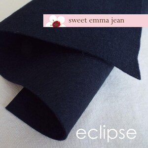 May include: A close-up of a dark blue felt fabric. The fabric is folded in half and the text "sweet emma jean" and "eclipse" is visible.