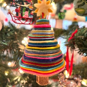 May include: A colorful, handmade Christmas tree ornament. The tree is constructed from stacked felt circles in various colors, topped with a yellow star. The ornament hangs from a red string, adding a festive touch to the holiday decor.
