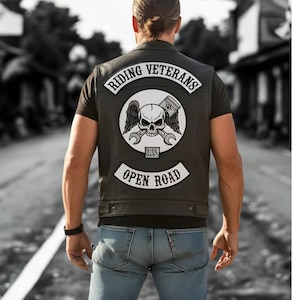 Può includere: Gilet in pelle nera con toppe. Le toppe recitano "RIDING VETERANS" e "OPEN ROAD". Una toppa centrale presenta un teschio con ali, un pistone e chiavi inglesi. Il gilet è indossato sopra una maglietta nera e jeans blu.