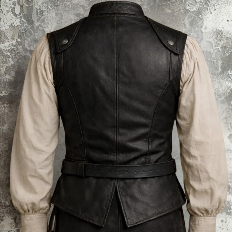Op de afbeelding: Zwart leren vest met een hoge kraag en een riem. Het vest heeft een getailleerde pasvorm met knoopdetails op de schouders. Het vest wordt gedragen over een cr&egrave;mekleurig shirt met lange mouwen.
