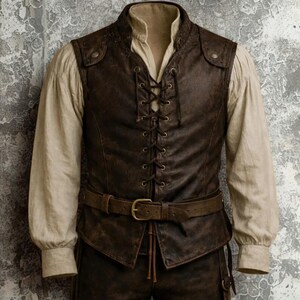 Op de afbeelding: Een bruin leren vest met een veter aan de voorkant en een bijpassende riem. Het vest wordt gedragen over een cr&egrave;mekleurig shirt met lange mouwen. De outfit heeft een vintage of historische uitstraling.