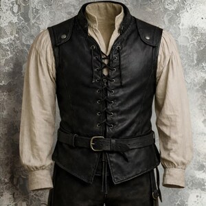 Op de afbeelding: Zwart leren vest met een veter aan de voorkant, een bijpassende riem en een hoge kraag. Het vest wordt gedragen over een cr&egrave;mekleurig shirt met lange mouwen. De stijl doet denken aan historische of fantasy kleding.