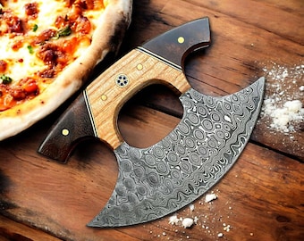 May include: A pizza cutter with a curved, patterned blade and a wooden handle. The handle features dark brown and light wood tones, with brass accents. The blade has a unique, swirling pattern. The cutter is on a wooden surface near a pizza.
