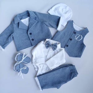 May include: A baby boy's outfit in blue and white. The outfit includes a jacket, vest, shirt, pants, bow tie, booties, and a hat. The vest has a white letter D embroidered on it.