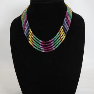 May include: Multi-strand necklace made of colorful gemstone beads. The necklace features five strands of beads in shades of green, blue, yellow, red, and black.