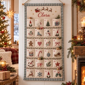 May include: A hanging fabric advent calendar with a blue and white gingham border, featuring twenty-four numbered pockets embroidered with Christmas motifs and the name Clara at the top, suspended from a wooden rod with a rope hanger.
