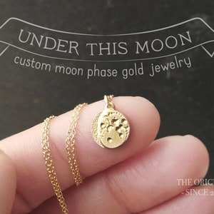 Op de afbeelding: Gouden ketting met een klein, rond hangertje met een gedetailleerd maanfasenontwerp. Het hangertje is getextureerd en heeft een gehamerde afwerking. De ketting is aan een delicate ketting. De tekst "UNDER THIS MOON custom moon phase gold jewelry" is zichtbaar boven de ketting. De tekst "THE ORIGINAL - SINCE 2012 -" is zichtbaar onder de ketting.