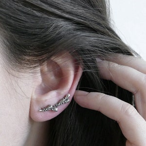 May include: Silver ear cuff with a delicate, leafy design. The cuff is curved and has a small, rounded end.